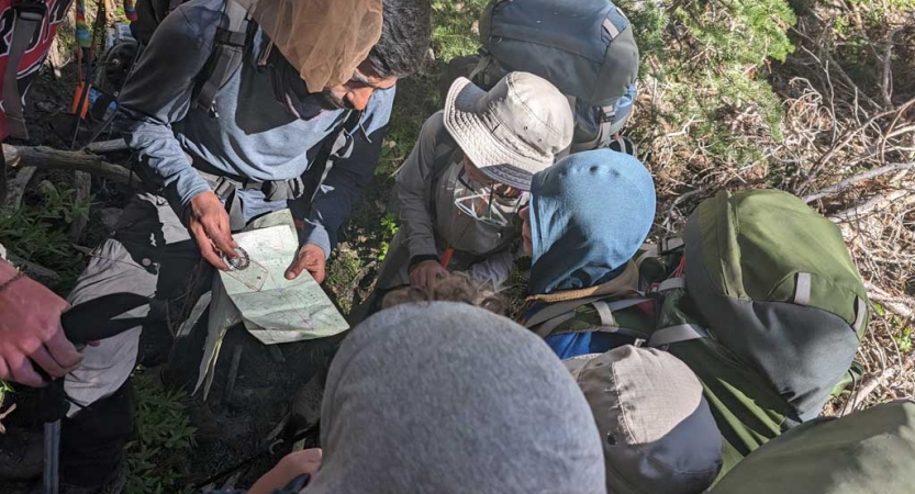 A group of backpackers examine a map and compass. 